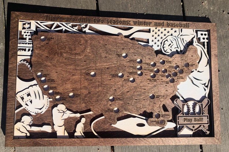 May include: A wooden map of the United States with a baseball theme. The map is decorated with baseball bats, a glove, and a baseball. The text "There are only two seasons: winter and baseball" is at the top of the map. The text "Play Ball!" is at the bottom of the map.