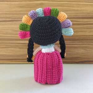 May include: A crocheted doll with black hair, a pink dress, and a colorful flower crown.