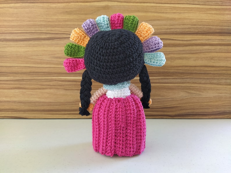 May include: A crocheted doll with black hair, a pink dress, and a colorful flower crown.