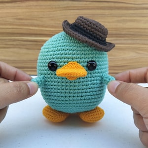 May include: A teal crocheted bird wearing a brown cowboy hat with orange feet.