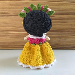 May include: A crocheted doll with black hair, a yellow dress with white trim, and a flower crown with pink and green flowers.