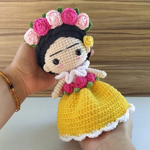 May include: Crocheted doll with a yellow dress, white lace trim, and a pink flower crown. The doll has black hair and a painted face.