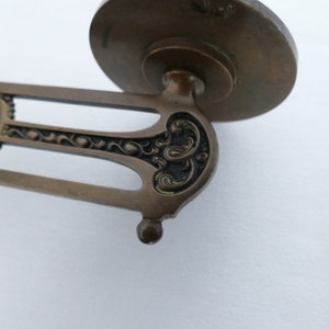 May include: A vintage brass wall sconce with an ornate design. The sconce has a round base and a decorative arm with a floral pattern.