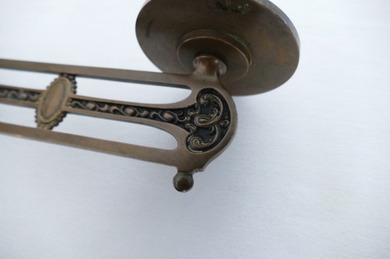 May include: A vintage brass wall sconce with an ornate design. The sconce has a round base and a decorative arm with a floral pattern.
