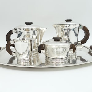 May include: A silver tea and coffee service set consisting of a teapot, a coffee pot, a creamer, and a sugar bowl with a lid, all featuring dark brown wooden handles and knobs, arranged on a matching silver serving tray with wooden side handles.