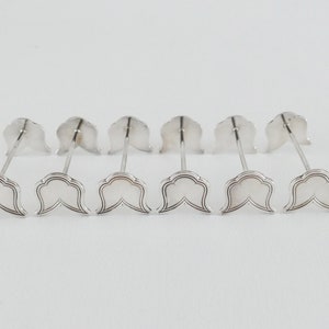 Op de afbeelding: Set van zes zilverkleurige servetringen met een decoratief, gegolfd ontwerp. Elke ring heeft een dunne, puntige steel.
