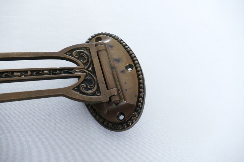 May include: A brass guitar strap button with an ornate design. The button has a hinge and is oval shaped.