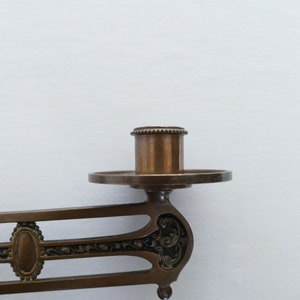 May include: A vintage brass wall-mounted candle holder with an ornate design. The holder has a single candle socket and a decorative base.