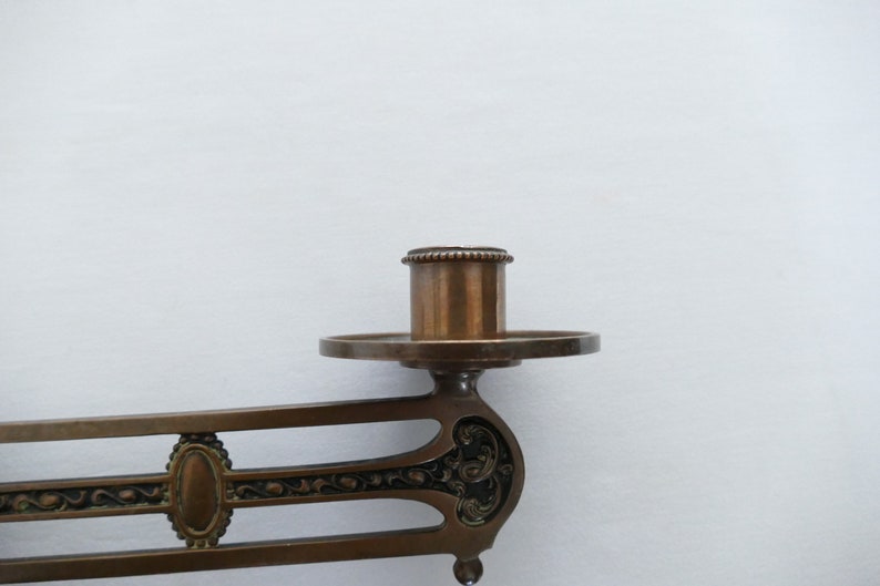 May include: A vintage brass wall-mounted candle holder with an ornate design. The holder has a single candle socket and a decorative base.