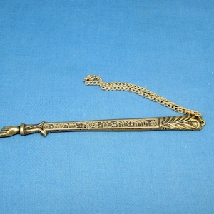 Puede incluir: Un abrecartas de bronce con un mango en forma de mano y un diseño decorativo. Tiene texto hebreo y una cadena dorada. El fondo es azul liso. Mide aproximadamente 15 cm de largo.
