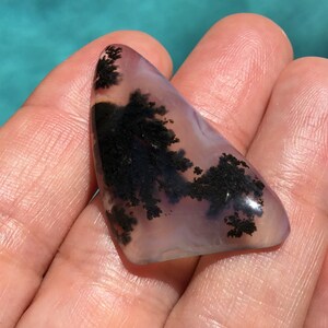 May include: A triangular shaped agate cabochon with dendritic patterns in black and white against a translucent purple background.
