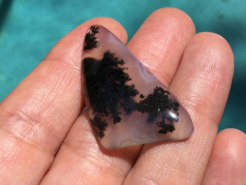 May include: A triangular shaped agate cabochon with dendritic patterns in black and white against a translucent purple background.