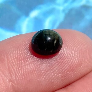 May include: A black gemstone with green and gold flecks, set in a round cabochon shape.