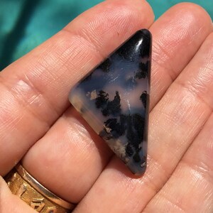 May include: A triangular shaped, black and white agate cabochon with a dendritic pattern. The cabochon is approximately 3.8 cm in length.