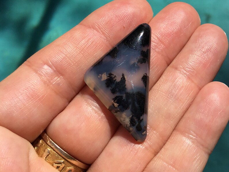 May include: A triangular shaped, black and white agate cabochon with a dendritic pattern. The cabochon is approximately 3.8 cm in length.