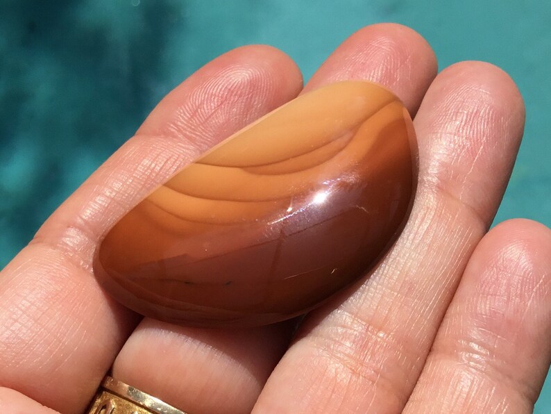 Pode incluir: Um caboch&atilde;o de &aacute;gata marrom polido e liso com bandas laranja e brancas. A pedra tem formato oval e um acabamento brilhante.