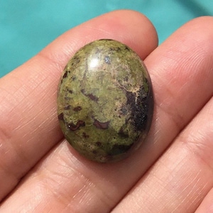 May include: A green and brown oval cabochon gemstone with a speckled pattern.