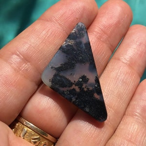 May include: A triangular shaped, black and white agate cabochon with a dendritic pattern. The cabochon is approximately 5 cm in length.
