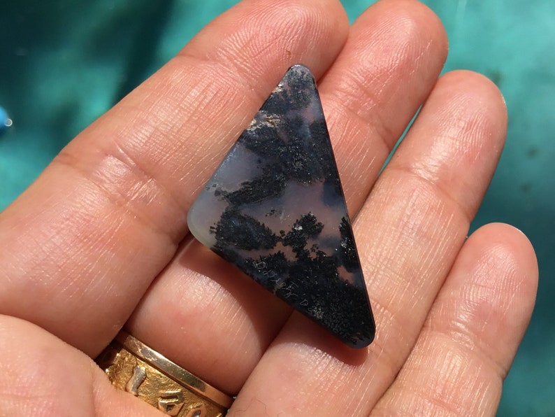 May include: A triangular shaped, black and white agate cabochon with a dendritic pattern. The cabochon is approximately 5 cm in length.