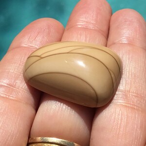 May include: A smooth, light brown stone with a swirling pattern of darker brown lines. The stone is polished and has a glossy finish.