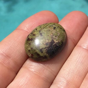 May include: A green and black oval cabochon gemstone with a smooth, polished surface.