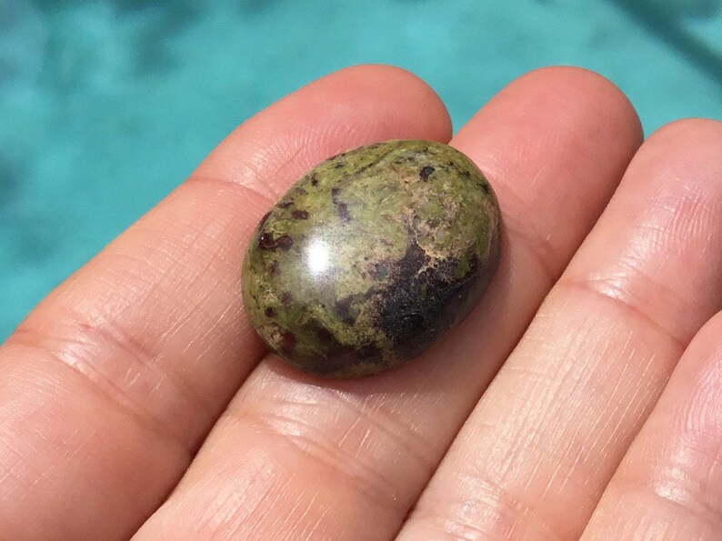 May include: A green and black oval cabochon gemstone with a smooth, polished surface.