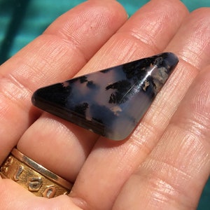 May include: A triangular shaped, polished, black and white agate cabochon with dendritic patterns. The cabochon is approximately 5 cm long.