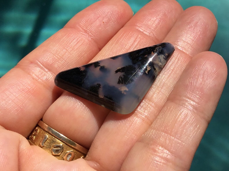 May include: A triangular shaped, polished, black and white agate cabochon with dendritic patterns. The cabochon is approximately 5 cm long.