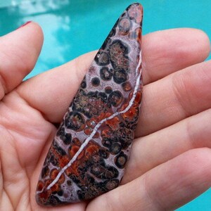 May include: A triangular shaped, polished, red, white, and black, agate stone with a white vein running through it.