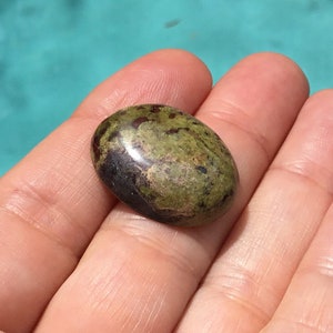 May include: A green and brown oval-shaped gemstone with red and black flecks. The gemstone is polished and smooth.