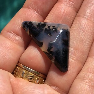 May include: A triangular, translucent, grey and black agate cabochon with dendritic inclusions. The cabochon is approximately 5 cm in length.