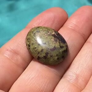 May include: A green and brown oval-shaped gemstone with a smooth, polished surface.