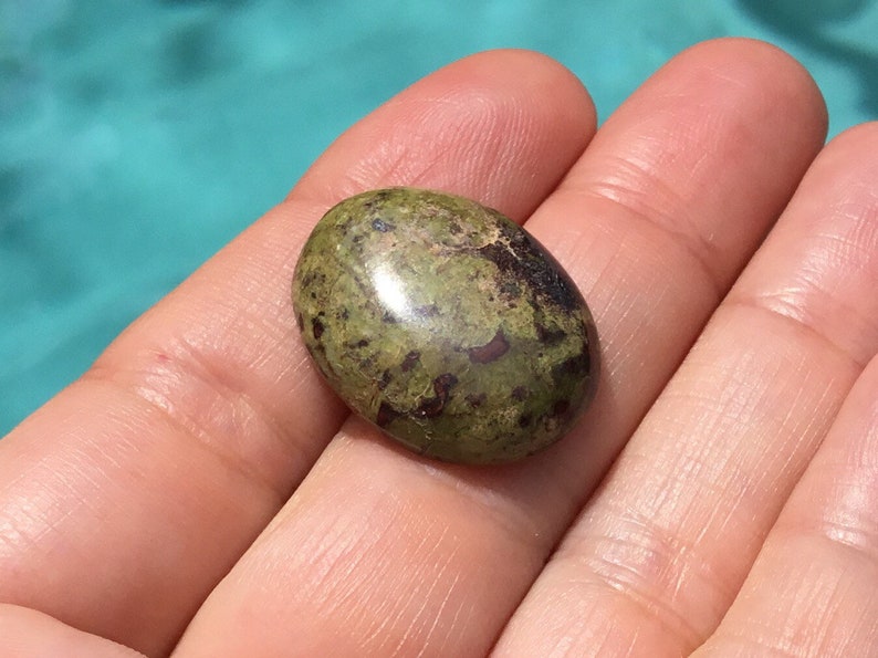 May include: A green and brown oval-shaped gemstone with a smooth, polished surface.