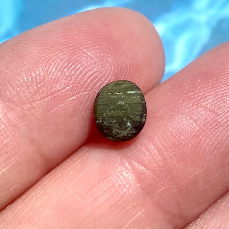 May include: A dark green oval-shaped gemstone with a shimmery, iridescent finish.