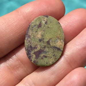 May include: A green, brown, and white oval cabochon gemstone with a mottled pattern.