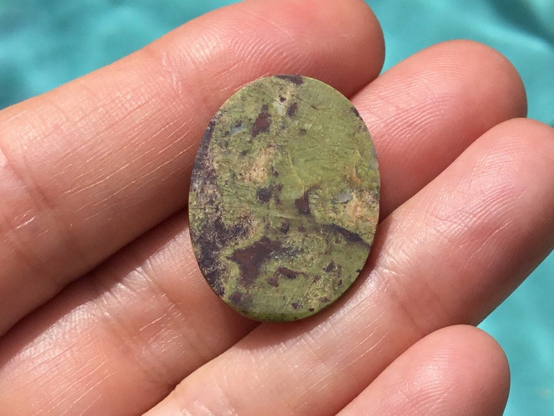 May include: A green, brown, and white oval cabochon gemstone with a mottled pattern.