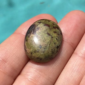 May include: A green and brown oval cabochon gemstone with a speckled pattern.