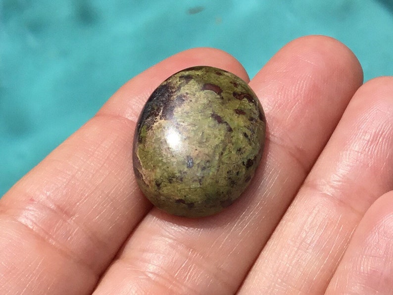 May include: A green and brown oval cabochon gemstone with a speckled pattern.