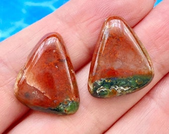 May include: Two triangular shaped red, green, and white agate cabochons. The cabochons are smooth and polished.