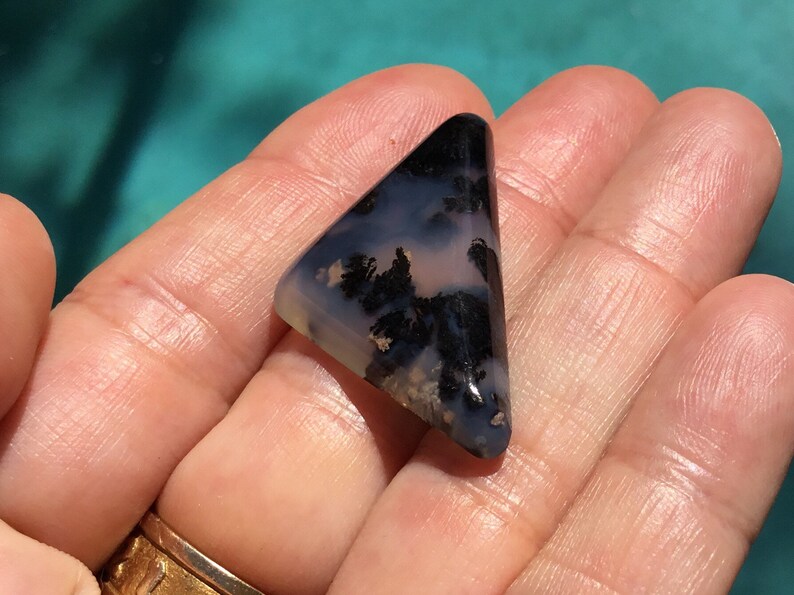 May include: A triangular shaped, polished agate cabochon with a dendritic pattern in black and white against a light blue and pink background.