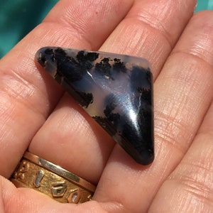 May include: A triangular shaped, polished, black and white agate cabochon with dendritic patterns. The stone has a glossy finish.