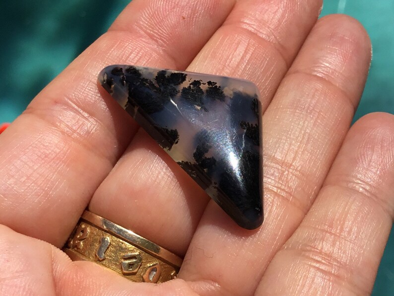 May include: A triangular shaped, polished, black and white agate cabochon with dendritic patterns. The stone has a glossy finish.