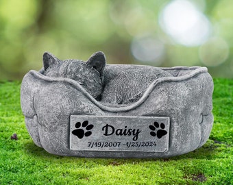 May include: A gray concrete pet memorial in the shape of a sleeping cat in a bed. The memorial has a plaque with the name "Daisy" and the dates "7/19/2007 - 1/25/2024".