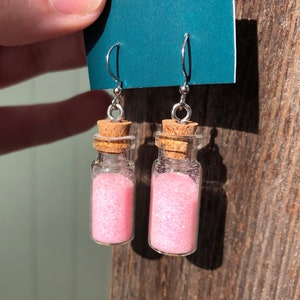 May include: A pair of pink glitter filled glass bottle earrings with cork stoppers and silver hooks.