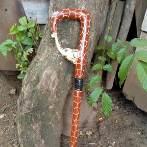 Puede incluir: Un bastón de madera con un diseño de estampado de jirafa. La parte superior del bastón está tallada en forma de cabeza de elefante.
