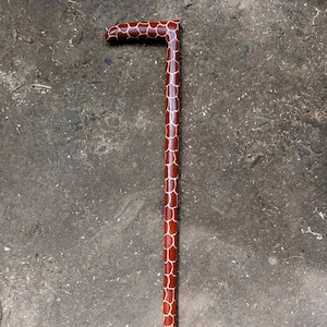 May include: A wooden walking stick with a giraffe print design. The stick is brown with white spots and has a black tip.