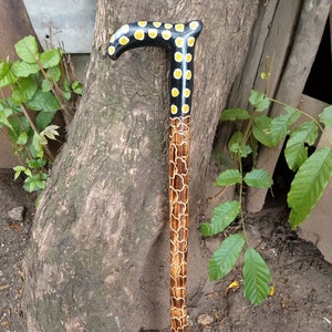 Può includere: Un bastone da passeggio in legno con un design a pois neri e gialli sul manico e un design a motivi marroni e bianchi sull'asta.