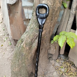 May include: A black wooden walking stick with a carved handle. The handle has a ring at the top and a detailed design.