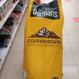 Puede incluir: Una bolsa amarilla de café Dormans Coffeehouse de Kenia, con un gráfico de montaña y el texto "The Coffee Experts". La bolsa es de 500g neto, tueste medio, molido medio, y tiene un sello de calidad de tueste con el texto "Since 1950".
