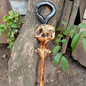 Puede incluir: Un bastón de madera con una cabeza de elefante tallada y un mango de anillo blanco y negro. El bastón es marrón y tiene un acabado de madera natural.